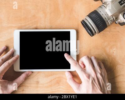 Blick von oben auf die männlichen Händen mit Tablet mit Kamera auf Holztisch. Stockfoto