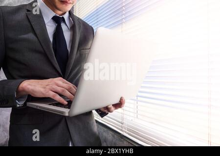 Nahaufnahme von Geschäftsmann mit Laptop während an einem Fenster stehen in einem Büro Stockfoto