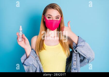 Foto von schönen Dame verwenden Organizer antiseptische Spray desinfizieren Arme in der Menge sozialen Orten Daumen Finger nach oben heben tragen Gesichtsmaske Denim Blazer gelb Stockfoto