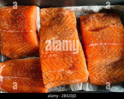 Einige Stücke Filet von rohem rotem Fisch mit Gewürzen liegen auf einem Backblech vor dem Rauchen, schwarzer Pfeffer und Salz, Lachs Stockfoto