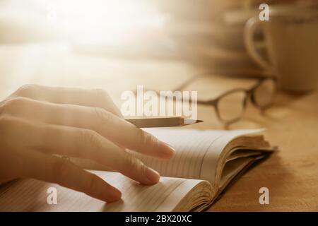 Nahaufnahme der männlichen Hand Schreiben in Notizbuch auf Holzschreibtisch, Soft Focus, Flare-Licht, Vintage-Ton. Stockfoto