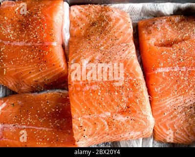 Einige Stücke Filet von rohem rotem Fisch mit Gewürzen liegen auf einem Backblech vor dem Rauchen, schwarzer Pfeffer und Salz, Lachs Stockfoto