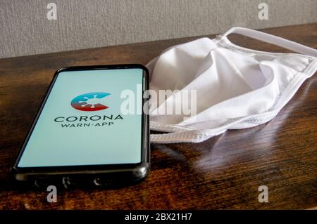 Zittau, Sachsen / Deutschland - 4. Juni 2020: Corona Virus Warn App für COVID-19 Tracing mit weißer Gesichtsmaske auf Holzfläche. Das neue normale, es Stockfoto