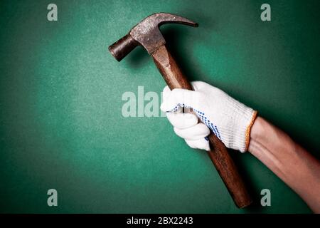 Hammer in die Hand mit Schutzhandschuh auf grünem Hintergrund. Freier Platz für Text Stockfoto