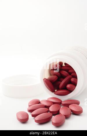 Rote Vitaminpillen, die aus der Flasche auf weißem Hintergrund ausgießen. Stockfoto