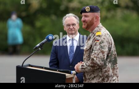 Burg, Deutschland. Juni 2020. Reiner Haseloff (CDU, l.), Ministerpräsident von Sachsen-Anhalt, sieht in der Clausewitz-Kaserne neben Fregatten-Kapitän Michael Hinz, Kommandeur des Logistik-Bataillons 171, eine Landesflagge. 150 Soldaten wurden mit einem Appell auf eine Auslandsmission nach Afghanistan entsandt. Der Einsatz des in Burg stationierten Logistik-Bataillons 171 ist Teil der NATO-Ausbildungsmission 'Resolute Support'. Kredit: Ronny Hartmann/dpa/Alamy Live News Stockfoto