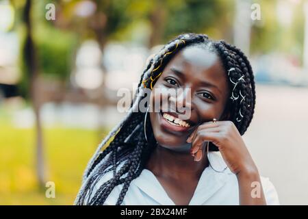 Nahaufnahme eines lächelnden jungen afroamerikanischen Mädchens mit Zöpfen. Sonniger Tag. Außenfoto. Stockfoto