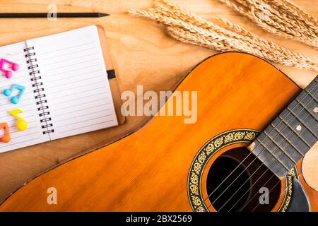 Draufsicht der Akustikgitarre mit leerem Notizbuch auf Holztischhintergrund. Stockfoto