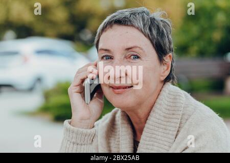 Glückliche ältere Frau auf den Straßen der Stadt mit Handy. Stockfoto