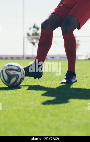 Die untere Hälfte des afroamerikanischen Fußballspielers tritt einen Ball Auf Gras Stockfoto