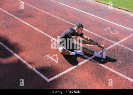Afroamerikanischer Athlet, der sich auf der Laufstrecke streckt Stockfoto