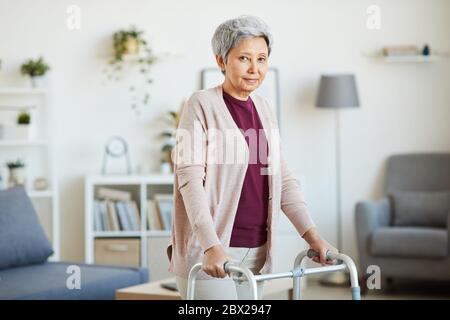 Porträt der schönen älteren Frau, die sich auf den Wanderer stützt und die Kamera anschaut, während sie im Raum steht Stockfoto