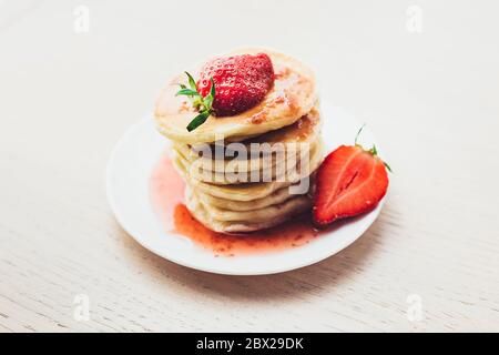 Ein Stapel von frisch duftenden heißen Pfannkuchen auf einem weißen Teller mit Erdbeermarmelade - frische Erdbeere gegossen Stockfoto