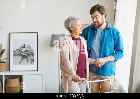 Ältere Frau mit Gehhilfe und im Gespräch mit ihrem Betreuer hilft er ihr während der Rehabilitation Stockfoto