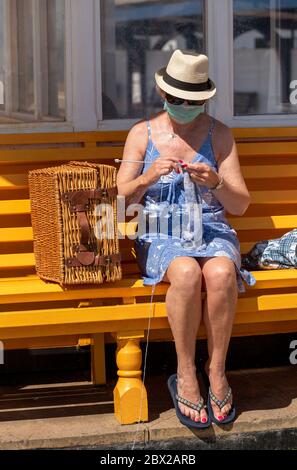 Southsea, Portsmouth, England, Großbritannien. 2020, Frau auf einer Bank am Meer, die während der Covid-19-Sperre einen Wollpullover strickt. Stockfoto