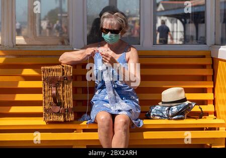 Southsea, Portsmouth, England, Großbritannien. 2020, Frau auf einer Bank am Meer, die während der Covid-19-Sperre einen Wollpullover strickt. Stockfoto