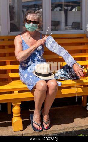 Southsea, Portsmouth, England, Großbritannien. 2020, Frau auf einer Bank am Meer, die während der Covid-19-Sperre einen Wollpullover strickt. Stockfoto