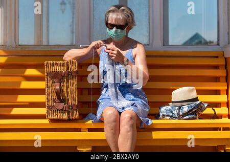 Southsea, Portsmouth, England, Großbritannien. 2020, Frau auf einer Bank am Meer, die während der Covid-19-Sperre einen Wollpullover strickt. Stockfoto