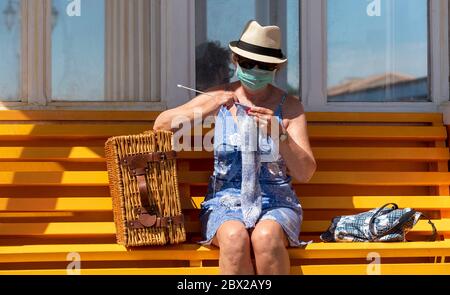 Southsea, Portsmouth, England, Großbritannien. 2020, Frau auf einer Bank am Meer, die während der Covid-19-Sperre einen Wollpullover strickt. Stockfoto