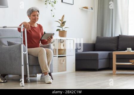 Ältere Frau auf dem Sofa sitzen und mit digitalen Tablet während im Wohnzimmer zu Hause ruhen Stockfoto