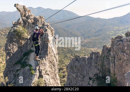 Konzept: Abenteuer. Frau mit Helm, Geschirr und Rucksack. Über den Abgrund auf einer tibetischen Brücke. Klettersteig in den Bergen. Stockfoto