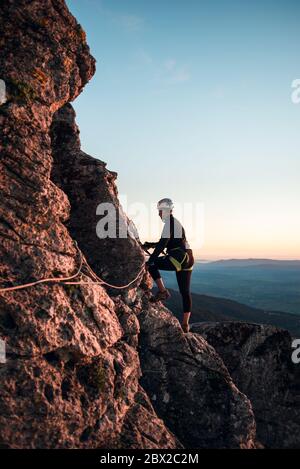 Konzept: Abenteuer. Kletterfrau mit Helm und Geschirr. Silhouette bei Sonnenuntergang auf dem Berg. Profil. Ruhe beim Blick auf die Kletterroute. Tun Stockfoto