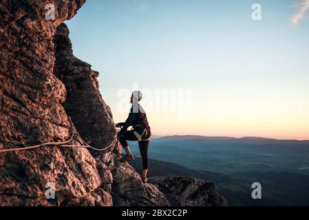 Konzept: Abenteuer. Kletterfrau mit Helm und Geschirr. Silhouette bei Sonnenuntergang auf dem Berg. Profil. Ruhe beim Blick auf die Kletterroute. Tun Stockfoto