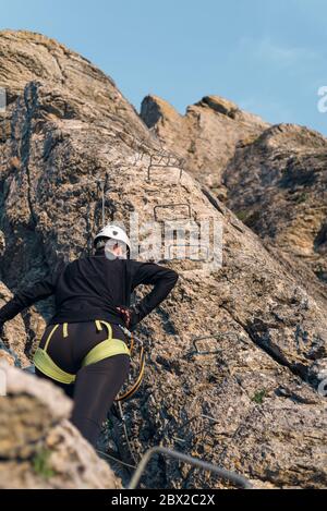 Konzept: Abenteuer. Kletterfrau mit Helm und Geschirr. Rückwärts. Ausruhen, bevor Sie weiter klettern. Klettersteig in den Bergen. Stockfoto