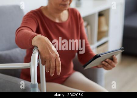 Nahaufnahme einer älteren Frau, die ein digitales Tablet hält und sich etwas darauf anschaut, während sie im Zimmer sitzt Stockfoto