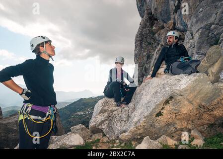 Konzept: Abenteuer. Drei Bergsteiger mit Helm und Geschirr. Ein Mann und zwei Frauen. Ausruhen entspannt sitzen auf einem Felsen. Klettersteig in der Bergkuge Stockfoto