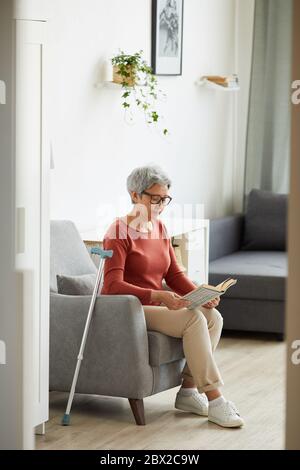 Ältere Frau in Brillen, die auf dem Sofa ruht und zu Hause ein Buch liest Stockfoto