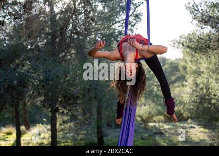 Junge akrobatin. Üben von Luftseiden. Starke Frau, die Zirkusstunts mit Kleidung im Wald macht. Candy Cane Trick Pose. Stockfoto