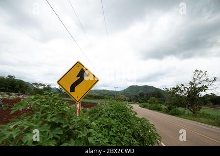 Gelbe Verkehrsschilder warnen vor kurvenreichen Straßen vor grünem Gras im Hintergrund Stockfoto