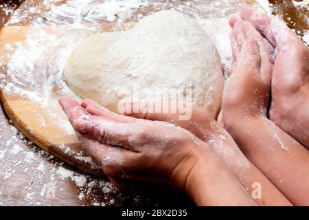 Teig aus Eiern und Milch machen. Herzförmiger Teig mit weiblichen und kindlichen Händen. Kochen und Home Konzept Stockfoto