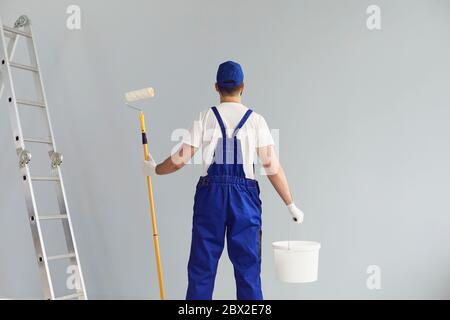 Rückansicht des Reparaturarbeiters, der Bürstenrolle und Eimer mit Farbe hält. Professionelle Auftragnehmer renovieren Haus Stockfoto