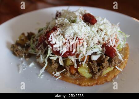 Enchilada oder Tostada aus Honduras mit Carne molida, Kartoffeln, Karotten, Ketchup, Salsa, gebratenen Tortilla und honduranischem Käse Stockfoto