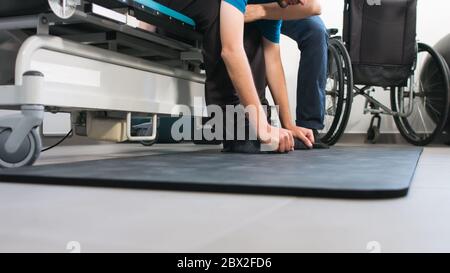 Physiotherapeut, der mit behinderten Menschen im Rollstuhl auf einem Therapietisch trainiert. Stockfoto