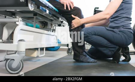 Physiotherapeut, der mit behinderten Menschen im Rollstuhl auf einem Therapietisch trainiert. Stockfoto