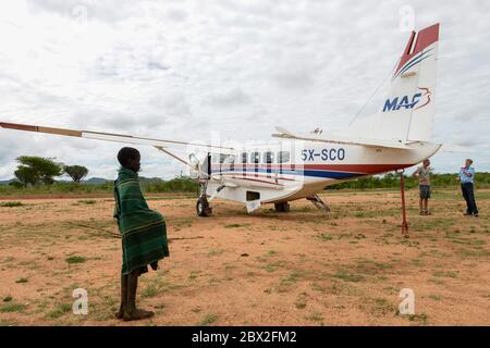 UGANDA, Karamoja, Kaabong, Karimojong Boy und Cessna Aircraft of MAF Mission Aviation Fellowship, a Airline for Missionars, NGO, Humanitary Aid / MAF Flugzeug auf dem Airstrip Stockfoto