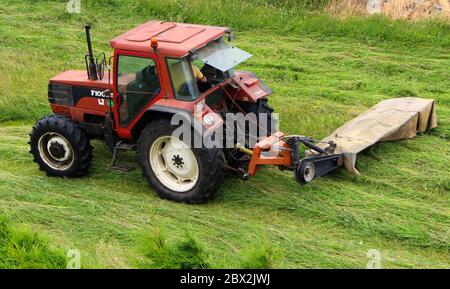 Milchviehtraktor mit Schlepplift hinter dem Scheibenmäher zum Schneiden von Gras Santander Cantabria Spanien Stockfoto