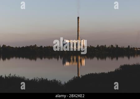 Alte Müllverbrennungsanlage am Ufer des Sees. Alte Müllverbrennungsanlage mit Rauchschornstein. Dunkler Hintergrund Stockfoto