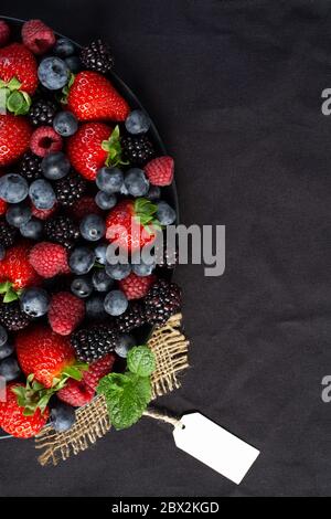 Erdbeeren, Brombeeren, Himbeeren, grüne Minze auf Leinwand und schwarzer Hintergrund mit Geschenkanhänger. Mock Up, Menü, Cafe Poster Konzept Stockfoto