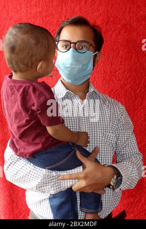 Vater trägt chirurgische Maske im Gesicht und tragen sein Baby Sohn spielen zusammen, Vatertag Konzept während Corona-Virus, covid-19 auf rotem Hintergrund Stockfoto