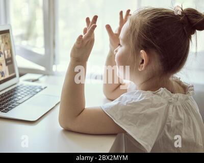 Nettes kleines Mädchen mit Laptop zu Hause. Bildung, Online-Studium, Zuhause das Mädchen zu Hause kommuniziert mit Freunden im Internet. Kinder Fernunterricht. Hochwertige Fotos Stockfoto
