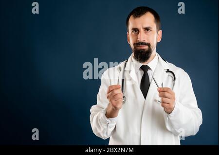 Porträt des männlichen Arztes mit Stethoskop in medizinischer Uniform hält in seinen Händen zahnärztliche Instrumente posiert auf einem blauen isolierten Hintergrund. Stockfoto