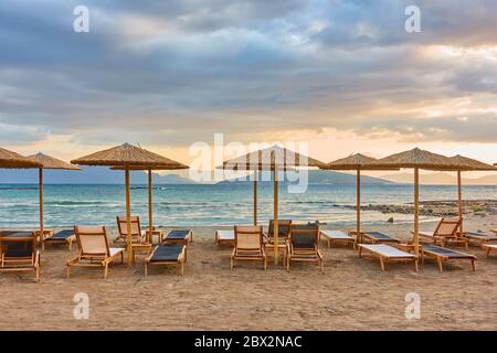 Strand mit Reihen von Strohschirmen bei Sonnenuntergang, Insel Ägina, Griechenland - griechische Landschaft Stockfoto