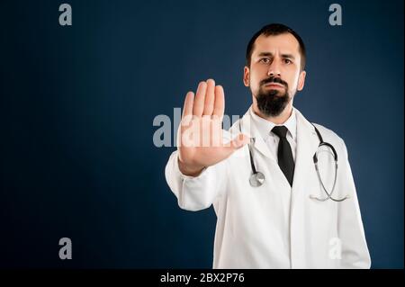 Porträt des männlichen Arztes mit Stethoskop in medizinischer Uniform mit Stoppschild posiert auf einem blauen isolierten Hintergrund. Stockfoto