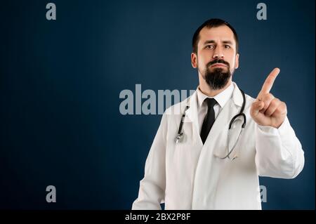 Porträt des männlichen Arztes mit Stethoskop in medizinischer Uniform, das Nein zeigt, mit dem Finger auf einem blauen, isolierten Hintergrund posiert. Stockfoto