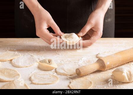 Vorderansicht der weiblichen Hände halten Fleischknödel mit Holz-Nudelholz auf einem Holztisch mit Mehl bestreut. Der Prozess der Zubereitung von hausgemachten Ravioli, Stockfoto