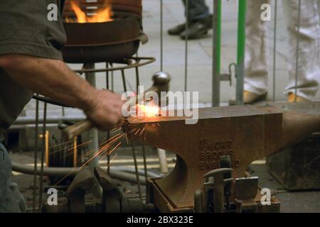 Metallbearbeitung - Mann schlägt beheizte Stahlstange mit einem Hammer auf einem traditionellen Eisenanvil (Schmied) Stockfoto